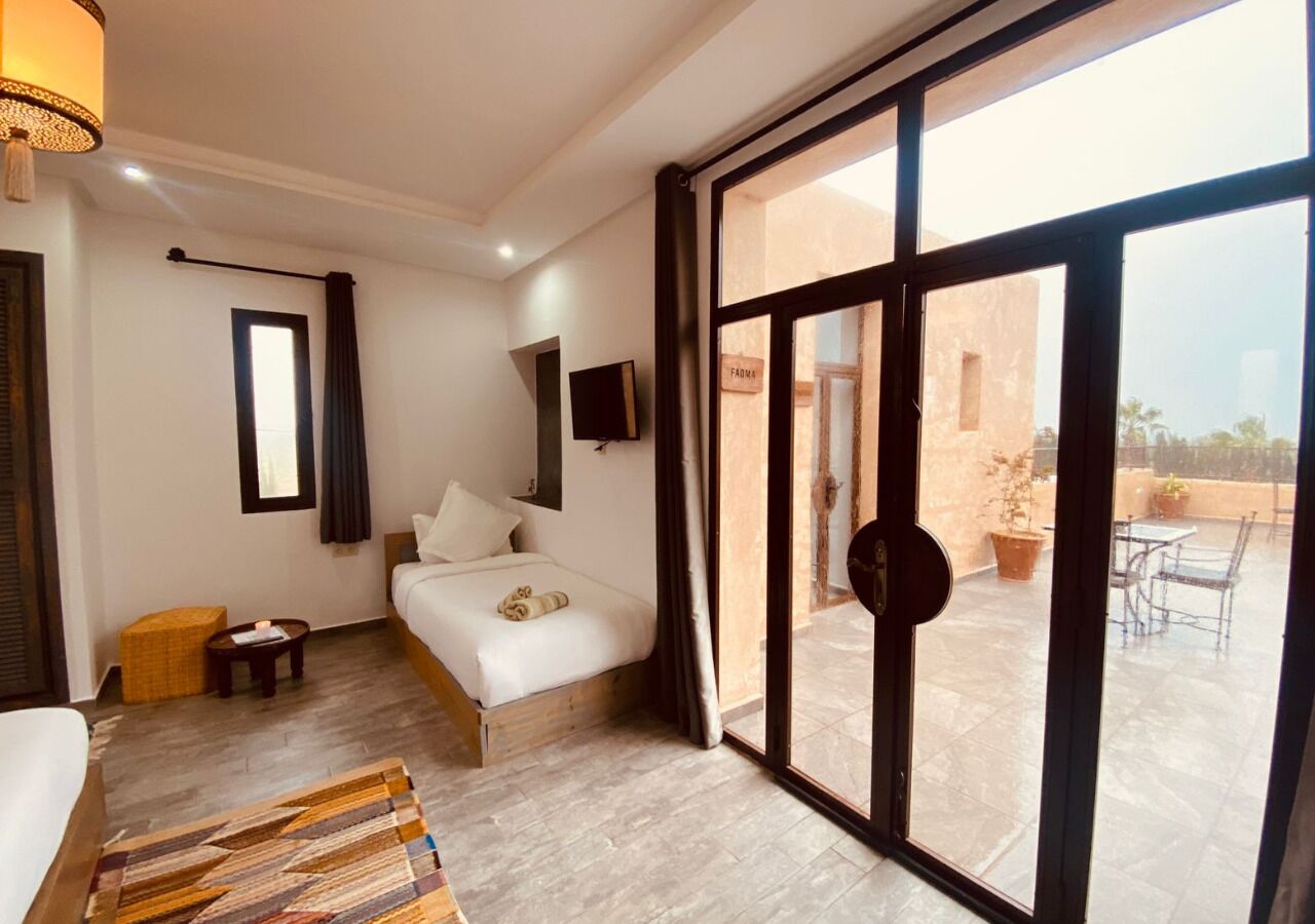 A hotel room with a bed, a small table, a chair, a sofa, a window, and a view of the outside.