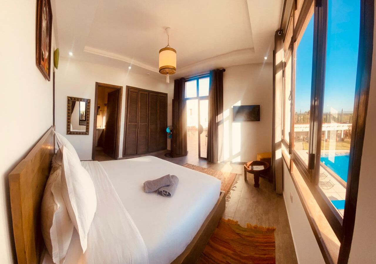 A hotel room with a large bed, a view of a swimming pool, and a door leading to a balcony.