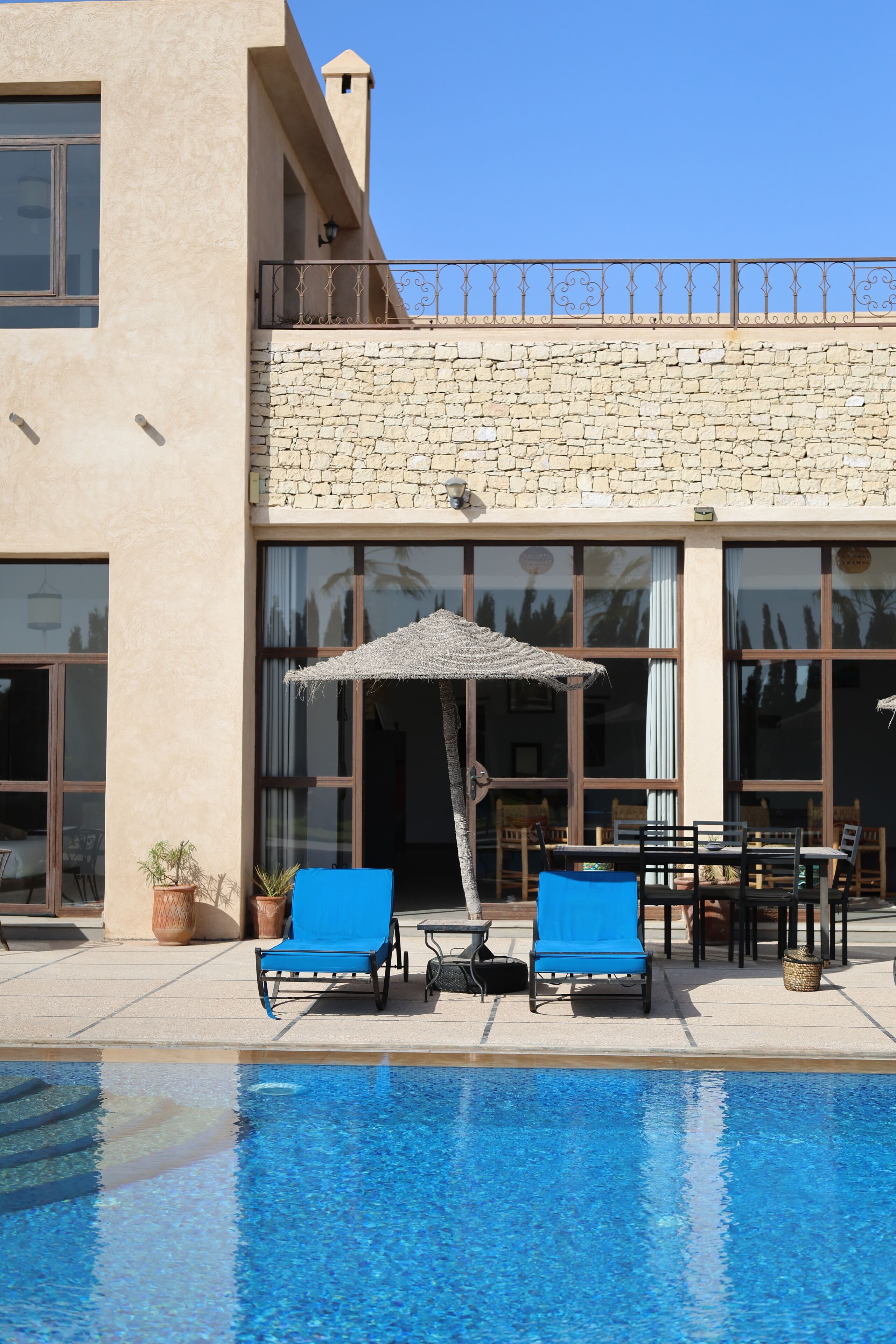 A poolside area with two blue lounge chairs, a table, and an umbrella.