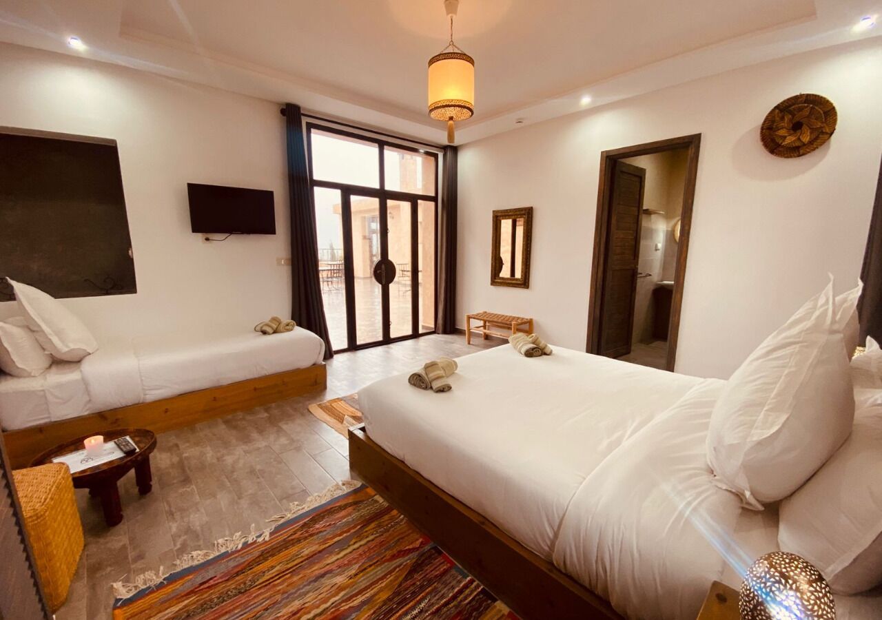 Habitación de hotel con una cama grande, un sofá más pequeño, televisor, espejo y ventana con vistas.