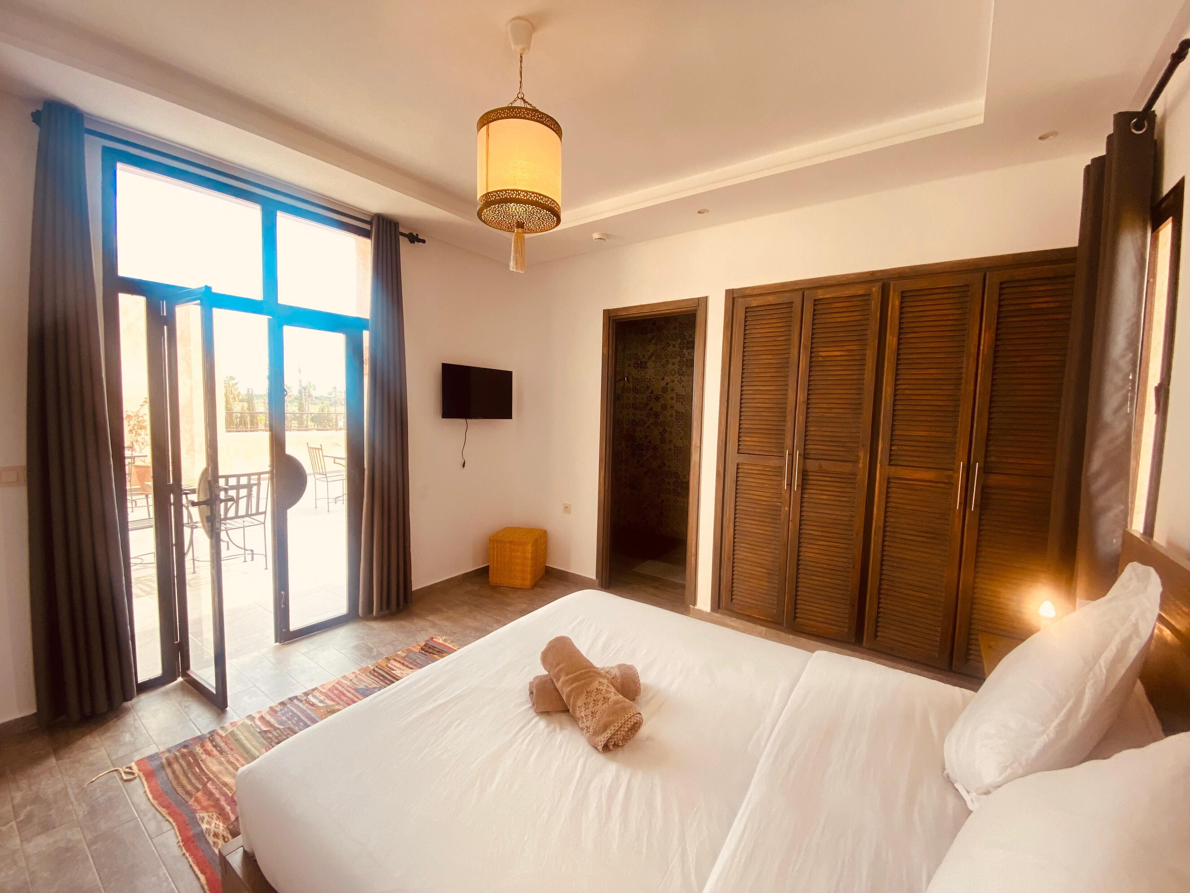 A hotel room with a large bed, a television, a wardrobe, and a balcony with a view.