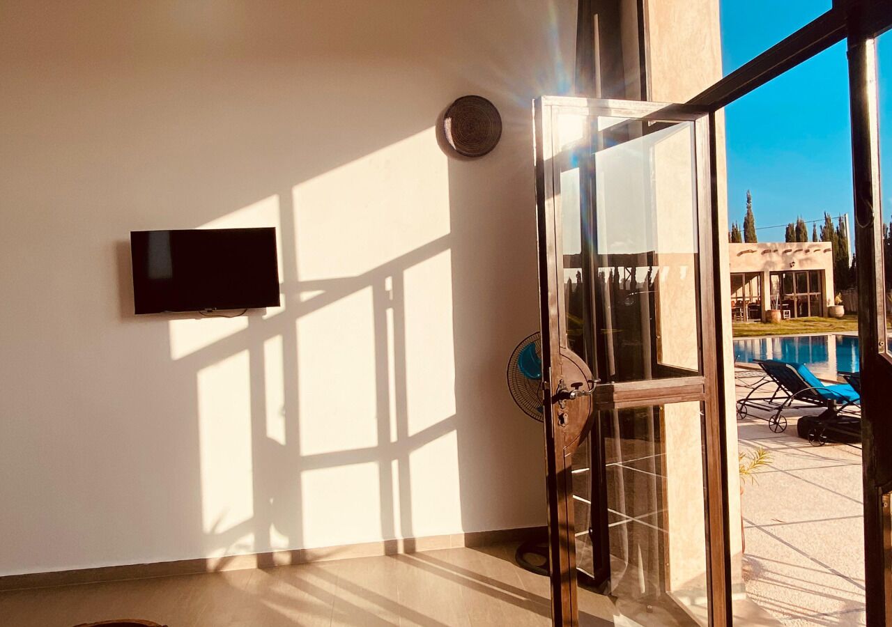 Een moderne kamer met een grote glazen deur die leidt naar een zwembad, een flatscreen televisie aan de muur en een plafondventilator.