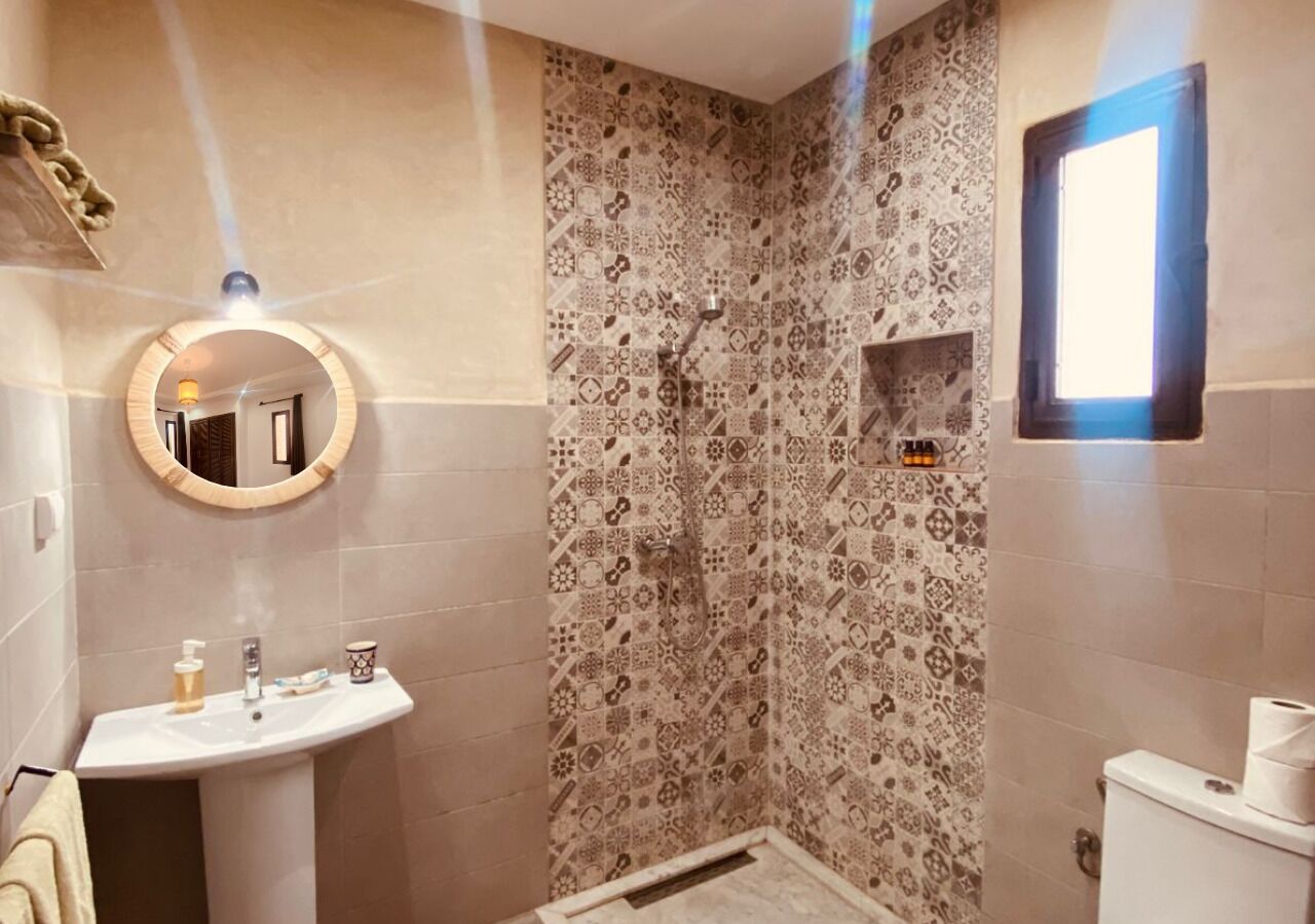 Un baño con ducha, lavabo, espejo y baldosas estampadas.