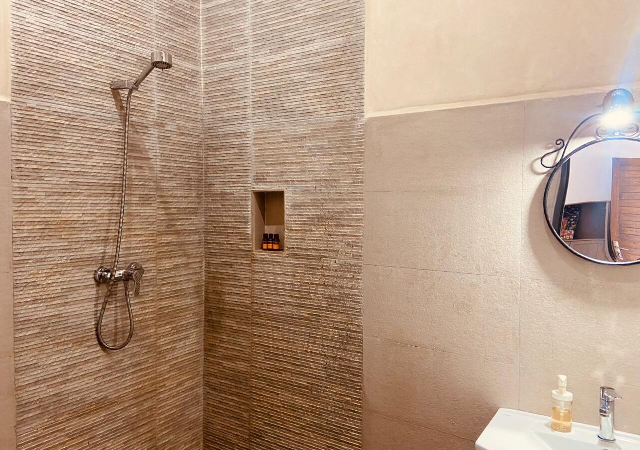 Ein Badezimmer mit Dusche, einer kleinen Ablage für Toilettenartikel und einem Spiegel.