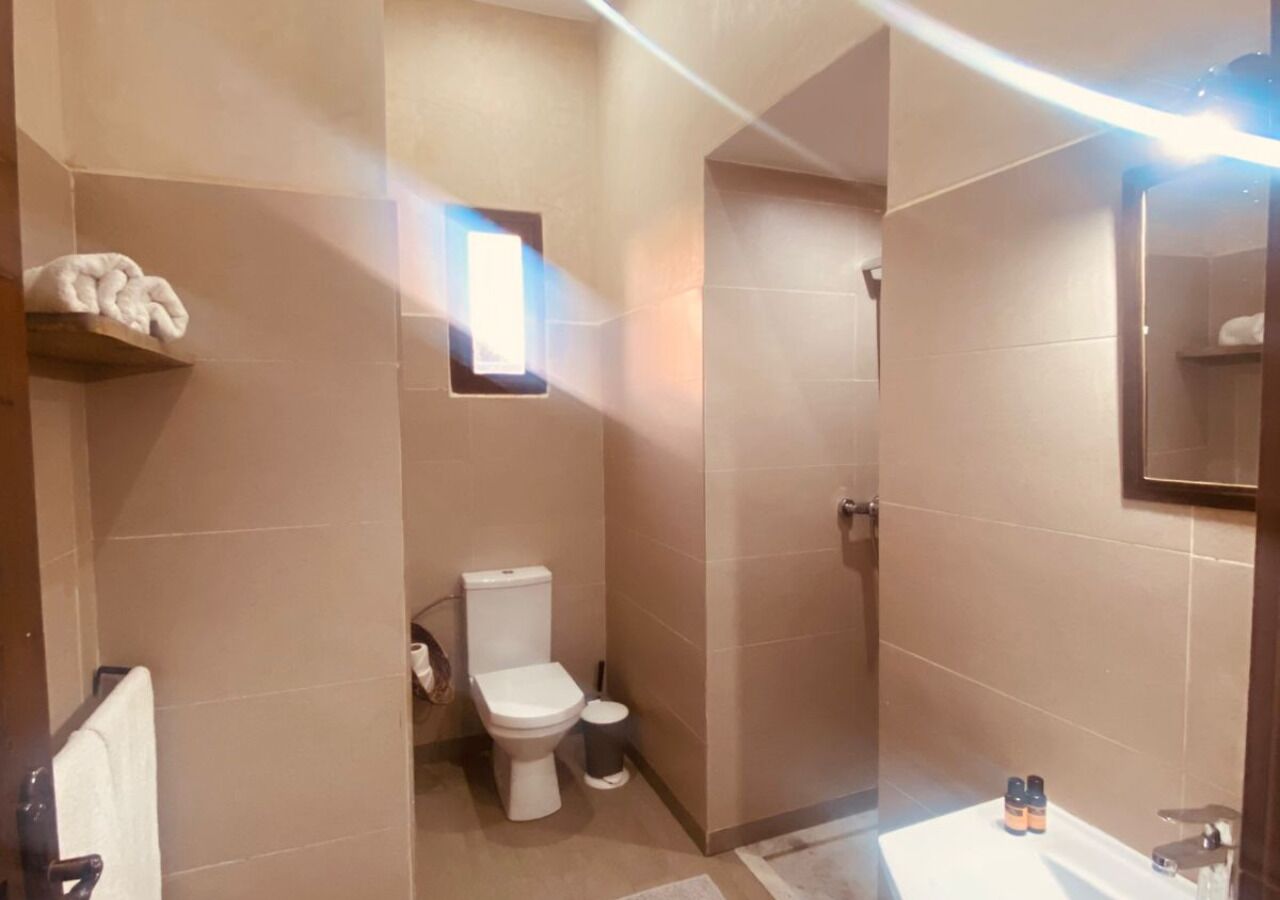 Un bagno con il water, un lavandino e uno specchio. C'è un porta asciugamani e una piccola finestra.