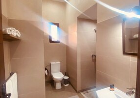 Un bagno con il water, un lavandino e uno specchio. C'è un porta asciugamani e una piccola finestra.