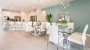 A modern kitchen with white cabinets, stainless steel appliances, and a dining area with a glass table and white chairs. - Last Minute Disney! Private Pool, Hot Tub, Game Room & Themed Bedrooms. Book Now! #47929 (Orlando)