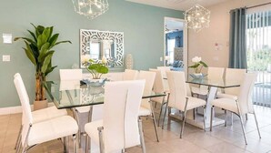 Zona pranzo con tavolo in vetro e sedie bianche, una pianta in vaso di grandi dimensioni e decorazioni murali.