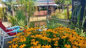 Een tuin met een rode ligstoel, een vijver en gele bloemen.
