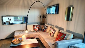 Een moderne woonkamer met een hoekbank, een houten salontafel, een vloerlamp en een raam met uitzicht op bomen.