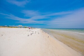 Una playa con cielo despejado, orilla de arena y edificios al fondo.