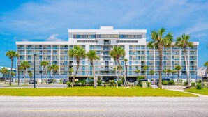 A multi-story hotel with a flat roof, balconies, and palm trees in the foreground. - Gulf Shores Surf & Racquet 614a 1 Bedroom Condo (Gulf Shores)