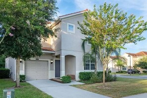 A two-story residential building with a garage, a small porch, and a well-maintained lawn.