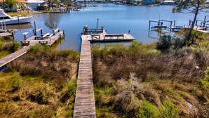 A marina with docked boats, a wooden walkway leading to the docks, and a calm lake. - At Ease - 535 Barcelona 3 Bedroom Home by RedAwning (Dauphin Island)