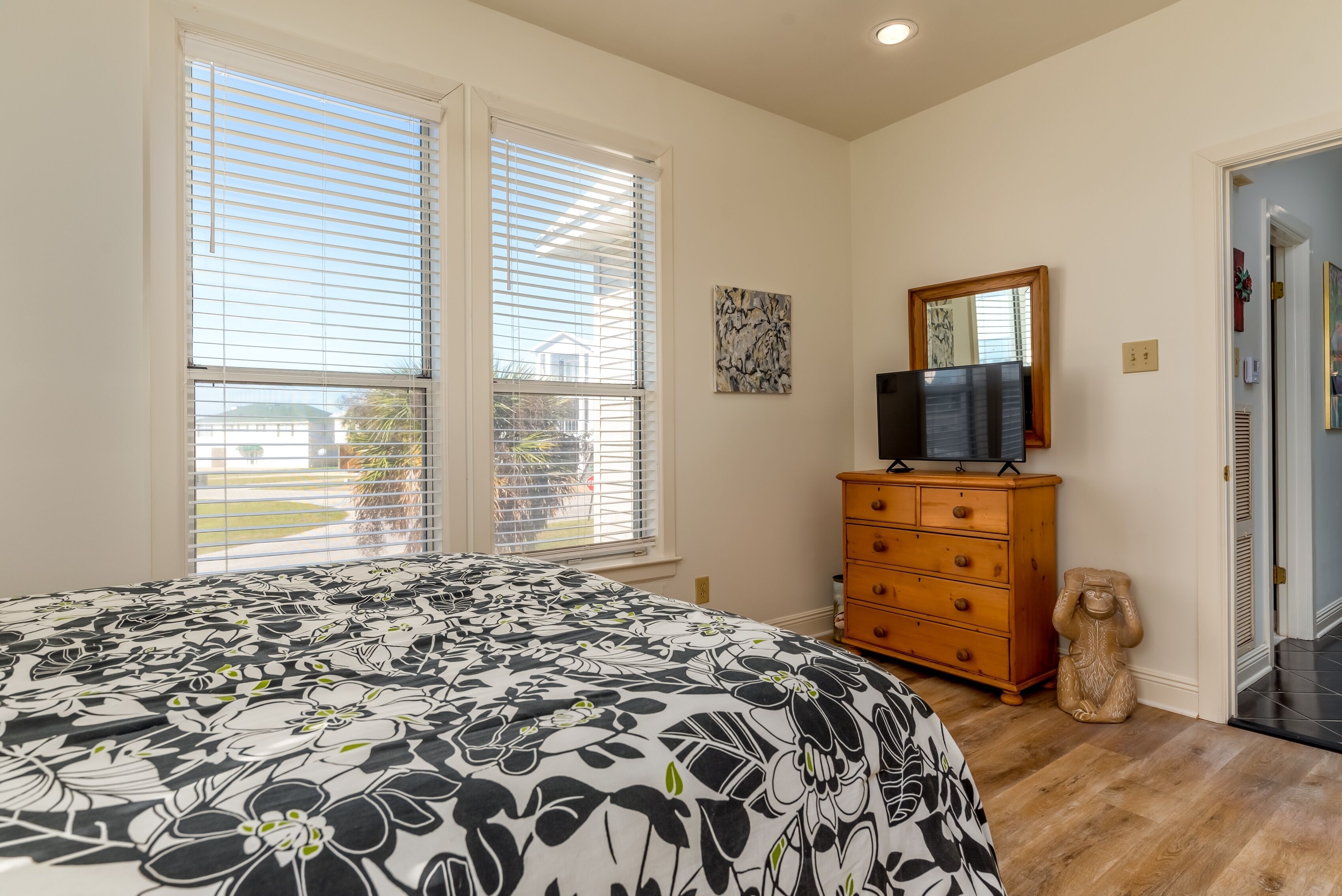 A bedroom with a large bed, a dresser, a television, and a window with blinds.
