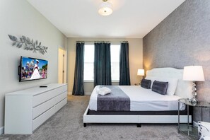 Ein Hotelzimmer mit Bett, Wandfernseher, Kommode und einem Vorhangfenster.
