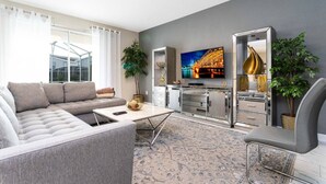 Un salon moderne avec un canapé gris, une table basse et un téléviseur diffusant une vue sur la ville.