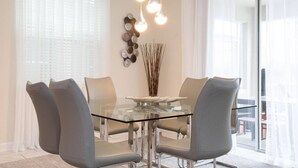 Un espace de salle à manger moderne avec une table en verre entourée de chaises grises, un élément décoratif mural et un luminaire suspendu.