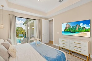 A bedroom with a large bed, a TV mounted on the wall, a sliding glass door to a balcony, and a white dresser. - Last Minute Disney Getaway! Luxury Villa with Private Pool. Book Now! #57975 (Orlando)