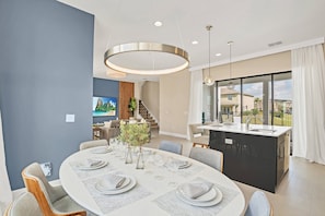 A modern dining area with a round table set for six, a kitchen island, and a view of the outdoors.