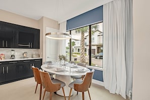 Une cuisine moderne avec des meubles noirs, un coin repas doté d’une table ronde et une vue sur l’extérieur grâce à de grandes fenêtres.
