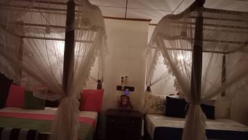 A room with two beds, each with a canopy. There are bedside tables with lamps and a small decorative item on one of them.
