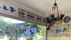 A balcony with wicker furniture, a stone wall with a fish mural, and hanging decorations. - Can Butik Pansiyon (Çesme)