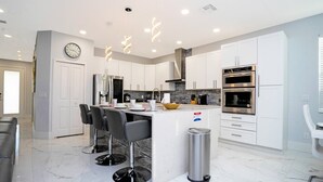 A modern kitchen with white cabinetry, a central island with bar stools, stainless steel appliances, and a marble floor. - Last Minute Disney Getaway! Private Pool, Hot Tub & Game Room. Book Now! #60493 (Orlando)