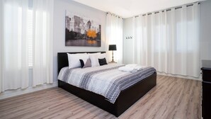 A modern bedroom with a large bed, white curtains, a cityscape painting, and a wooden floor. - Last Minute Disney Getaway! Private Pool, Hot Tub & Game Room. Book Now! #60493 (Orlando)
