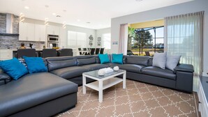 A modern living room with a sectional sofa, a glass coffee table, and a kitchen in the background. - Last Minute Disney Getaway! Private Pool, Hot Tub & Game Room. Book Now! #60493 (Orlando)