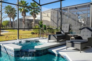 Piscina exterior coberta com hidromassagem, rodeada por mobiliário de vime e vista para palmeiras e uma casa.