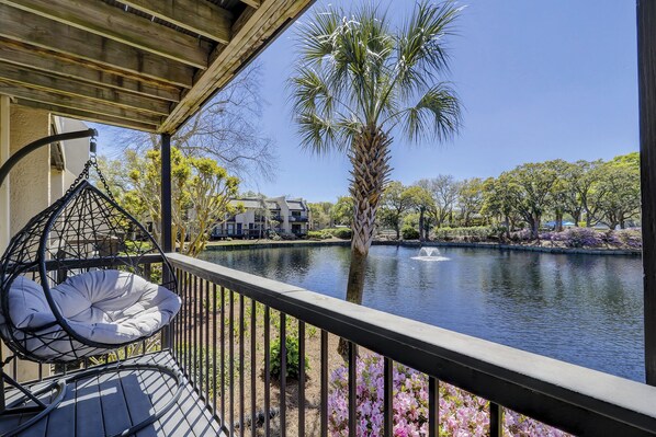 A balcony with a hanging chair, a palm tree, and a pond with a fountain.