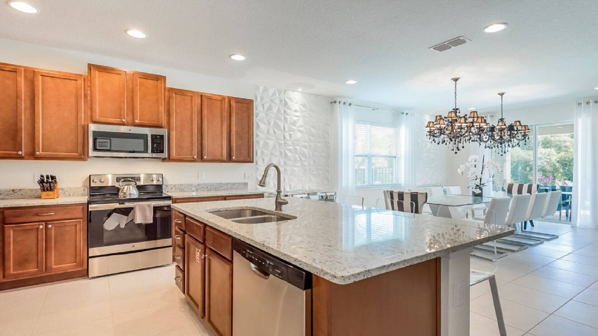 A modern kitchen with wooden cabinets, stainless steel appliances, a granite countertop, and a dining area with a glass table and chairs.