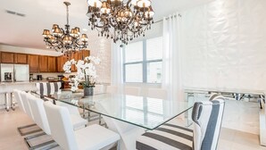Une cuisine moderne avec des meubles en bois, une table à manger en verre, des chaises blanches et un lustre.