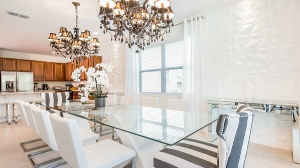 A modern kitchen with wooden cabinets, a glass dining table, white chairs, and a chandelier.