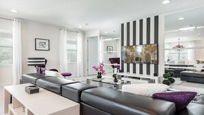 Un salon moderne avec un canapé d’angle, une table basse et un grand téléviseur à écran plat fixé sur un mur à rayures noires et blanches.