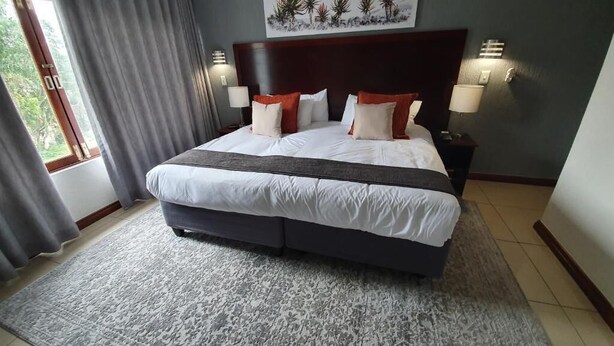 A large bed with white and red bedding, a dark headboard, and two bedside lamps. - Khayalami Hotel - Mbombela (Mbombela)