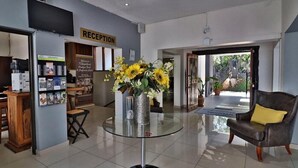 A reception area with a reception desk, a glass table with a vase of sunflowers, a leather chair with a yellow cushion, and a sign that reads "RECEPTION". - Khayalami Hotel - Mbombela (Mbombela)