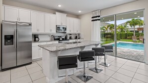 Una cocina moderna con armarios blancos, electrodomésticos de acero inoxidable y una zona de bar con taburetes.