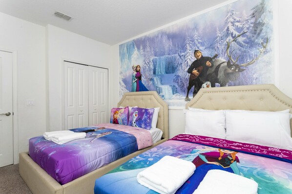 A bedroom with two beds, each with themed bedding and pillows, and a large mural of a winter scene on the wall.