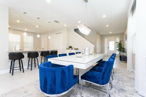 A modern dining area with a white table, blue upholstered chairs, and a chandelier.