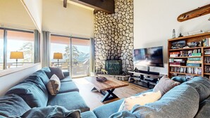 A living room with a stone wall, a TV, a bookshelf, and a sofa. - Bridges #308 4 Bedroom Condo by RedAwning (Mammoth Lakes)