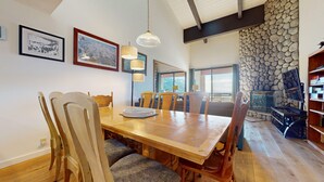 A dining area with a wooden table and chairs, framed pictures on the wall, and a stone wall in the background. - Bridges #308 4 Bedroom Condo by RedAwning (Mammoth Lakes)