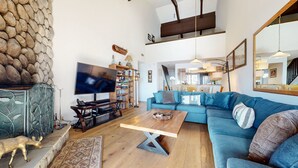 A living room with a TV, bookshelves, a blue sofa, and a wooden coffee table. - Bridges #308 4 Bedroom Condo by RedAwning (Mammoth Lakes)