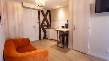 A modern kitchen with wooden accents, a dining area with a bar stool, and a large orange sofa.