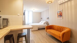 A modern kitchen with a wooden countertop, two black bar stools, a bed with white bedding, and an orange sofa. - Le Coursarlon (Bourges)