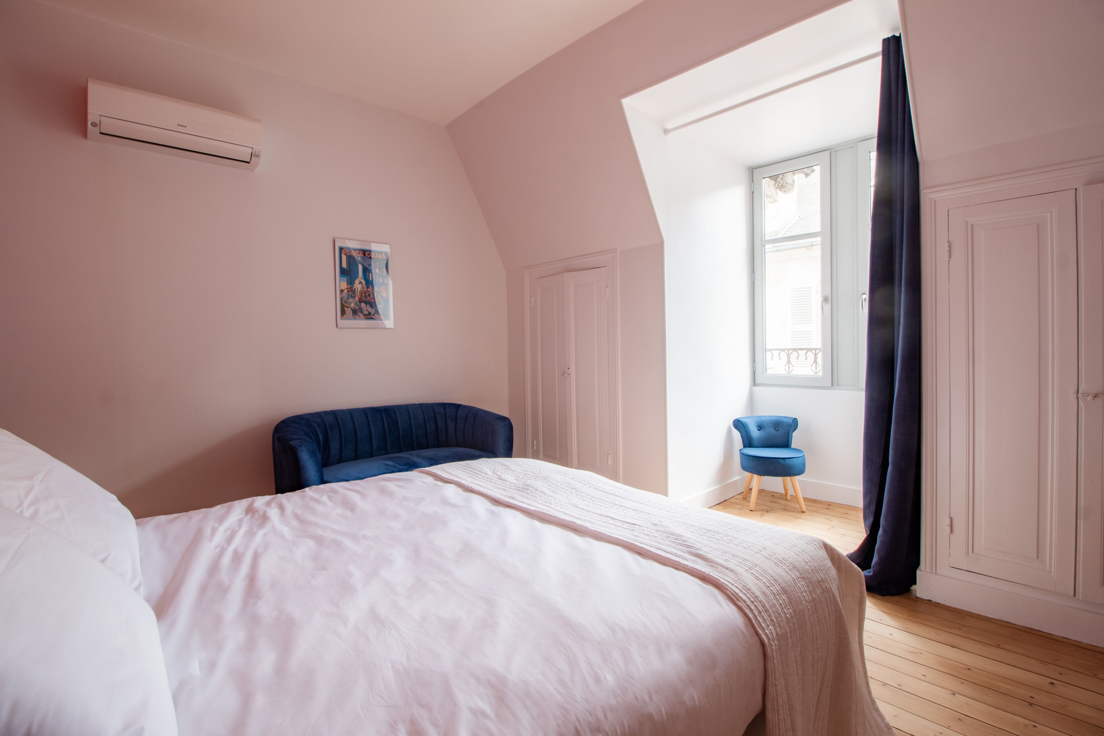A bedroom with a large bed, a blue chair, a small table, and a window with curtains.