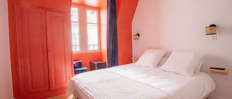 A bedroom with a large bed, a window with curtains, a wardrobe, and a small table.
