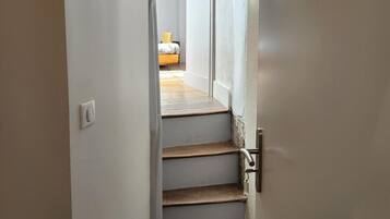 A narrow stairway leading to a bedroom with a bed and a window.