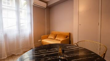 Una habitación con una mesa de mármol negro, una silla dorada, un sofá beige y una ventana con cortinas translúcidas.